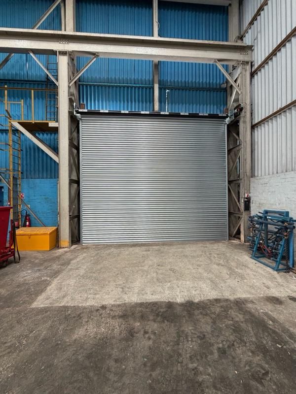 Closed silver roller shutter inside an industrial building with blue corrugated walls and steel beams.
