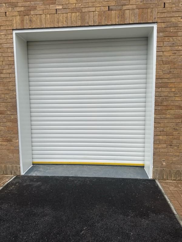 Closed white roller shutter recessed into a brick wall with a yellow strip along the bottom.