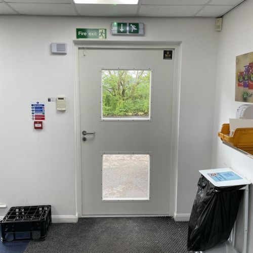 Grey glazed emergency exit door with vision panels in commercial building