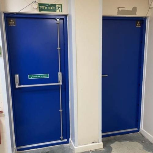 Blue steel fire exit door with push bar in commercial corridor